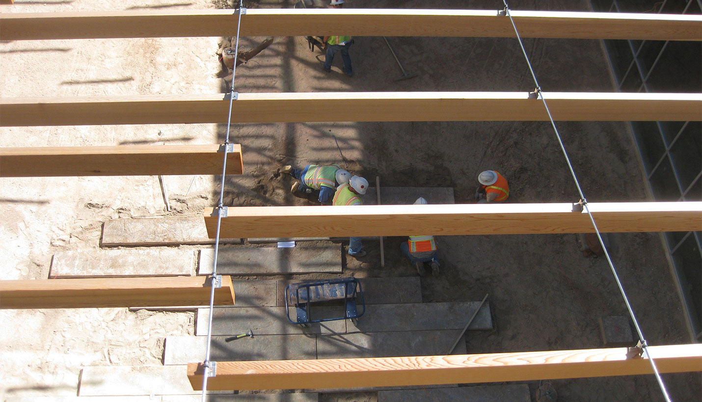 Most of the catenary structure was design/build. The designers assembled drawings but gave the contractor, Albuquerque’s Enterprise Builders Corp., leeway in how to install the shading system. Near the top of the east and west walls, the contractors used off-the-shelf hardware to attach 11 splice-welded eyebolts to ½-inch-diameter threaded rods. The rods are anchored with bolts and washers into grout in the concrete masonry unit back-up wall. After hanging the 11 cables, the contractors stabilized them with north-south lateral support cables, tying into each cable via a ¼” stainless steel cross-wire clamp. - 